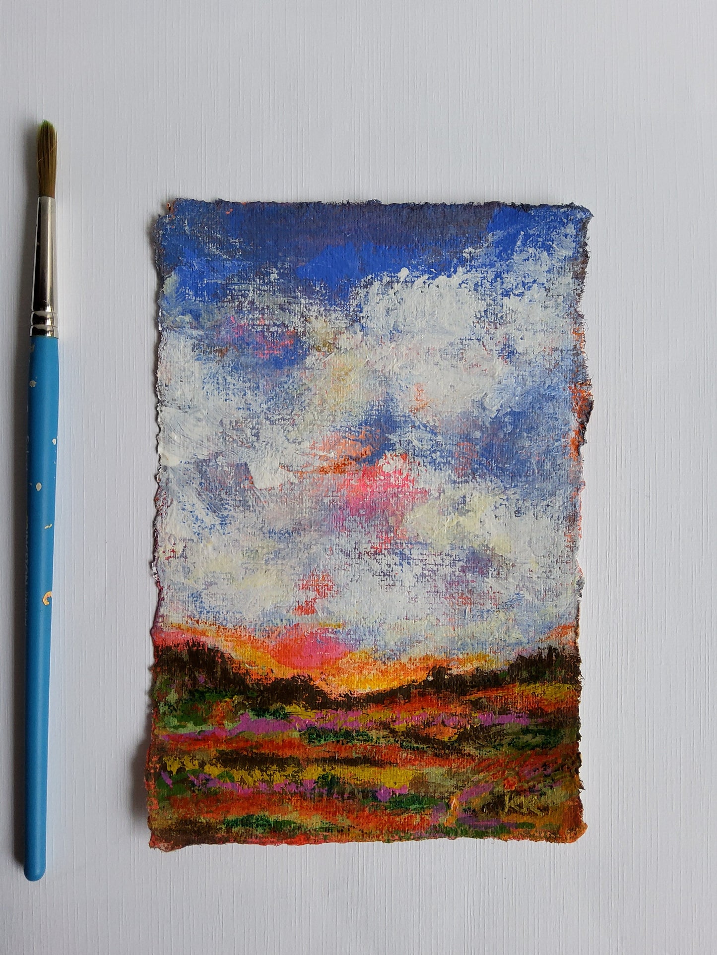 Colorful abstract painting on a textured surface with a blue paintbrush below.