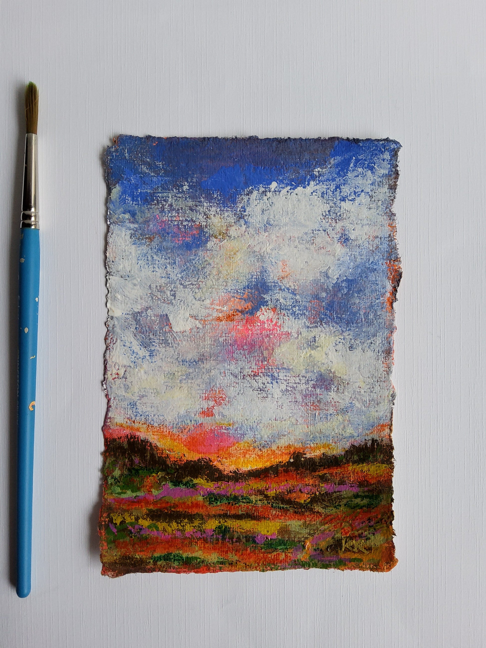 Colorful abstract painting on a textured surface with a blue paintbrush below.