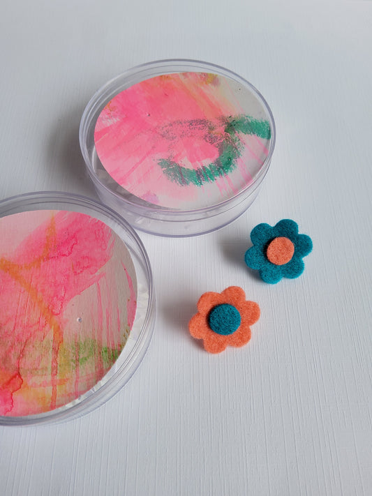 Two felt flower pins beside containers on a white background.