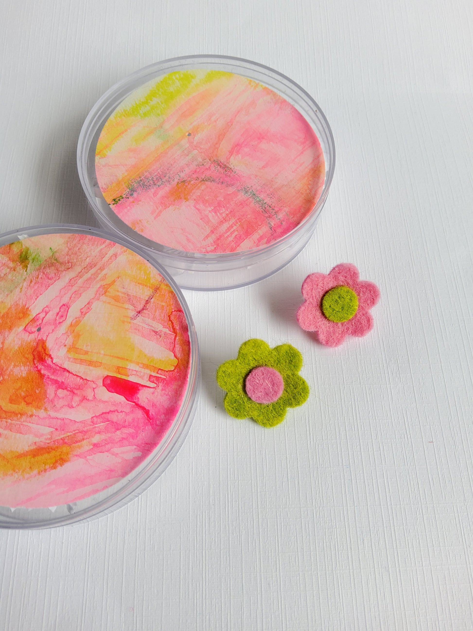 Two containers with colorful paint swatches and two felt flowers on a white background