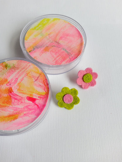 Two containers with colorful paint swatches and two felt flowers on a white background