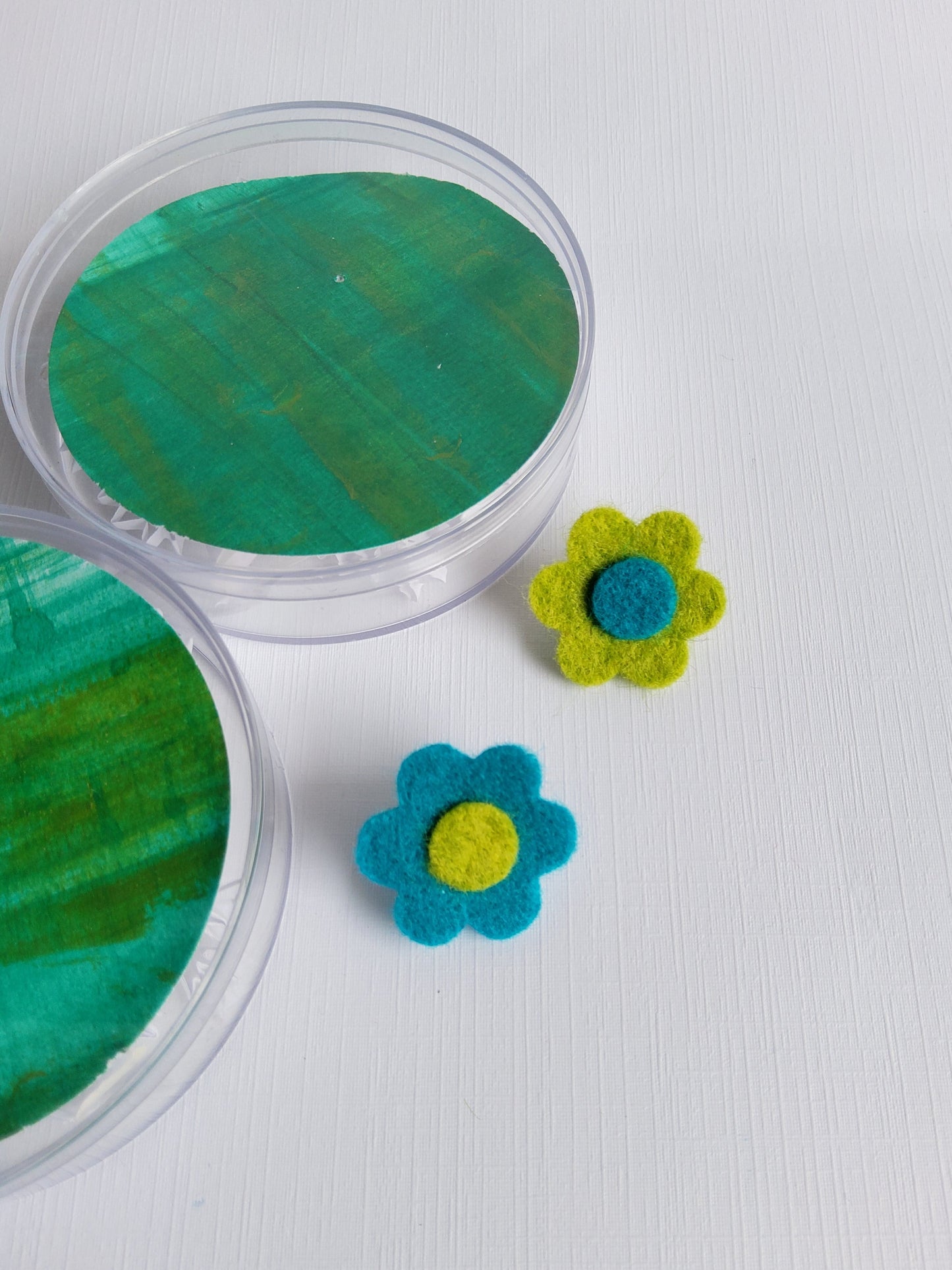 Two felt flowers, one green and one blue, on a white surface.