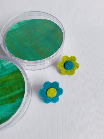 Two felt flowers, one green and one blue, on a white surface.