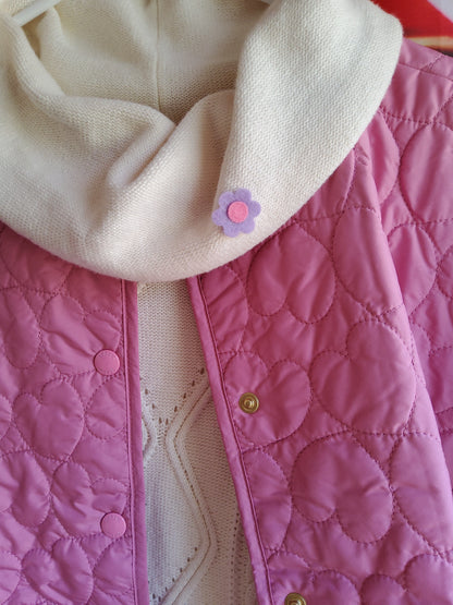 Close-up of felt flower pin on a cream color garment.