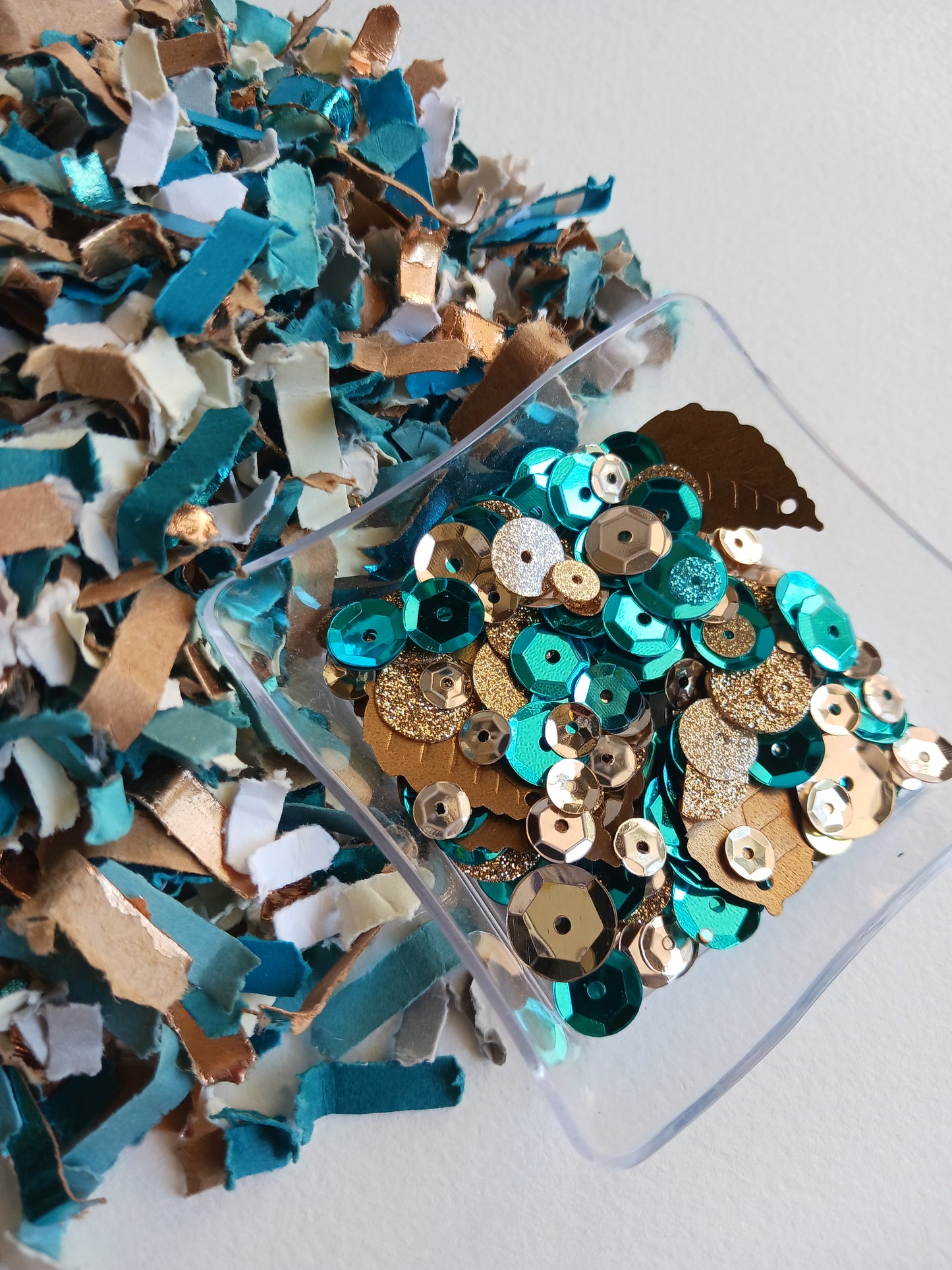 Colorful  blue, cream and gold confetti and  sequin mix on a clear plastic sheet against a white background 